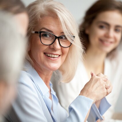 Smiling aged businesswoman in glasses looking at colleague at team meeting