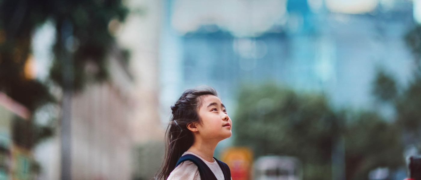Little girl looking up to the sky in front of buildings.