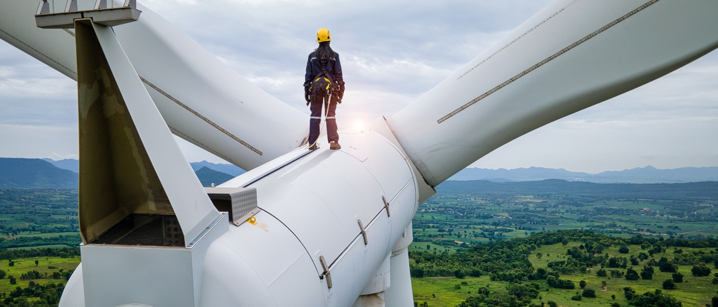 A female engineer strands on top of a wind turbine, looking at a beautiful landscape