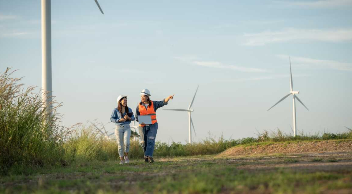 Deux femmes ingénieures marchent sur un chemin près d’un parc éolien. L’une d’entre elles pointe du doigt une éolienne