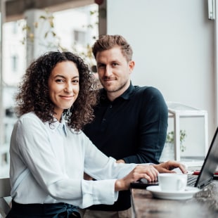 Une femme assise les mains sur le clavier de son ordinateur portable devant un homme accoudé à une table