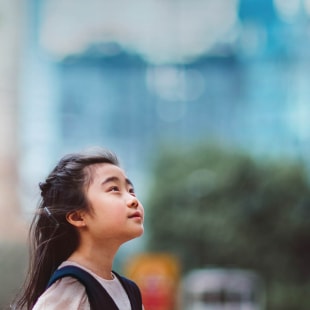 Petite fille regardant vers le ciel devant barre d'immeubles.