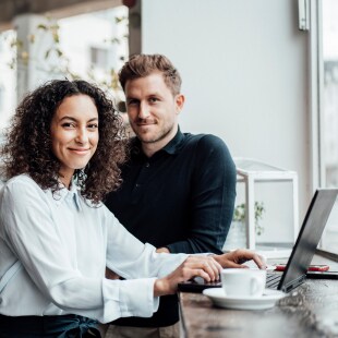 Une femme assise les mains sur le clavier de son ordinateur portable devant un homme accoudé à une table