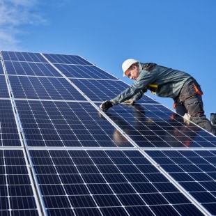 Photo d'un ouvrier masculin portant un uniforme, debout sur une échelle, en train d'installer des panneaux solaires