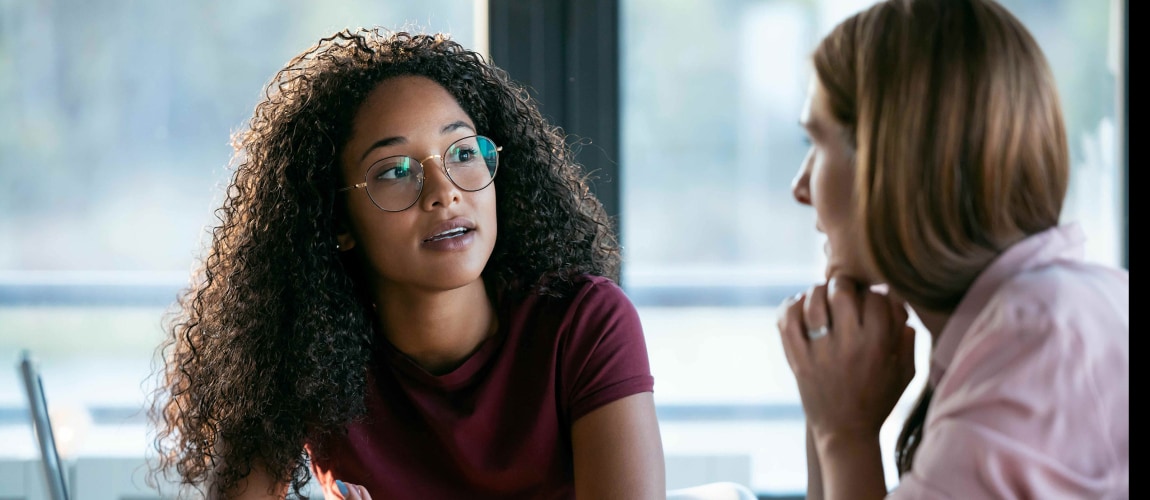 Two business women working together with laptop while talking about job news in the office.