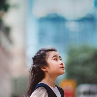 Little girl looking up to the sky in front of buildings.