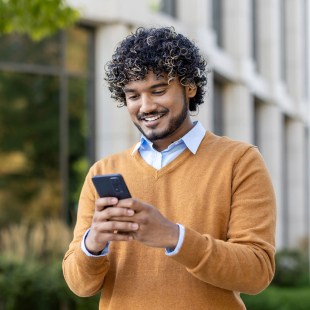 Jeune homme bouclé regardant son portable dans la rue.