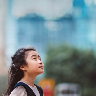 Little girl looking up to the sky in front of buildings.