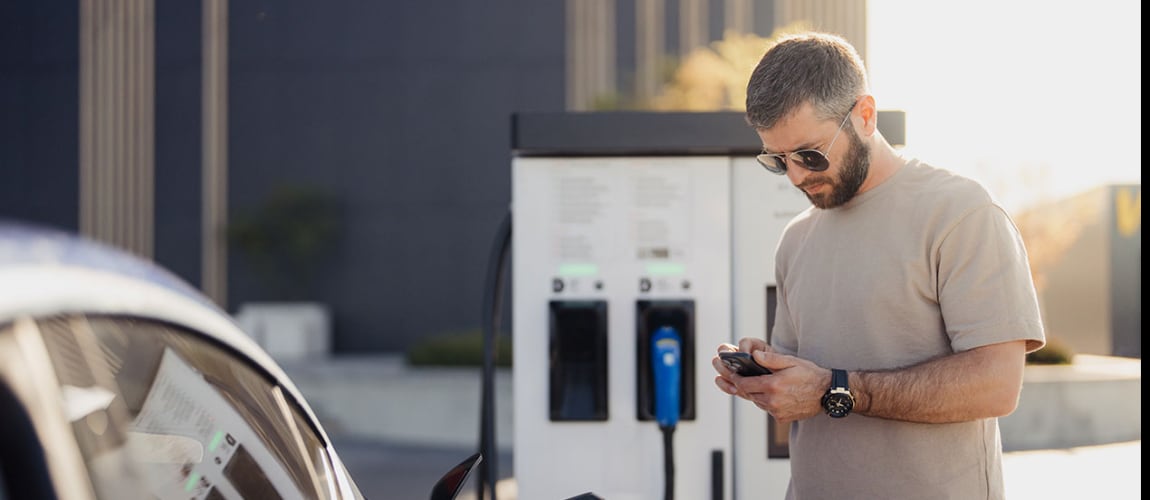 Homme qui regarde son téléphone portable devant une voiture et borne de rechargement