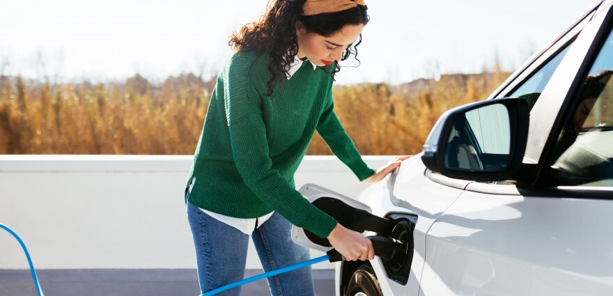 Une jeune femme charge sa voiture électrique à une station