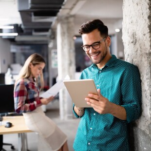 1 homme regarde une tablette adossé contre un mur