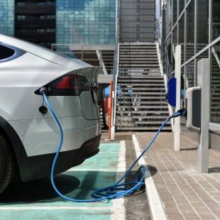 Voiture éléctrique branchée sur borne devant immeuble architecture corporate verre et acier