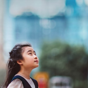 Little girl looking up to the sky in front of buildings.
