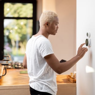 Young man choosing temperature on thermostat.
