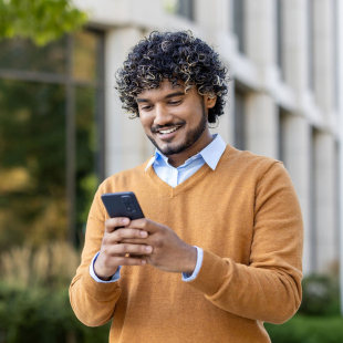 Young professional with curly hair using smartphone outdoors.