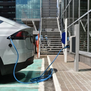 Voiture éléctrique branchée sur borne devant immeuble architecture corporate verre et acier