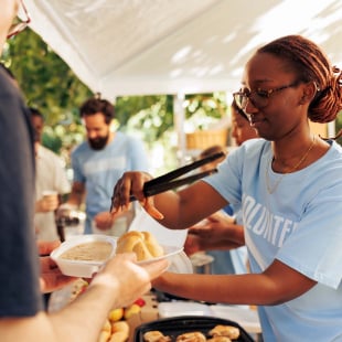 Image détaillée d’une femme noire lors d’une collecte de nourriture partageant des repas chauds gratuits à un pauvre sans-abri caucasien. Dans le centre local, un groupe de bénévoles nourrit et soutient les affamés et les défavorisés