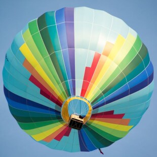 Envol d'une montgolfière multicolore sur fond de ciel bleu.