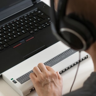 Blind person working on computer with braille display and screen